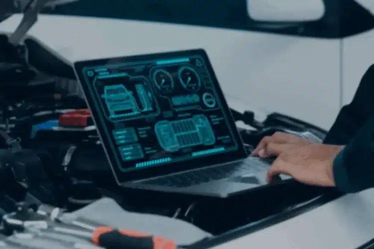 A person working on a laptop displaying automotive diagnostics, with a car engine in the background, illustrating React Native automotive app development.