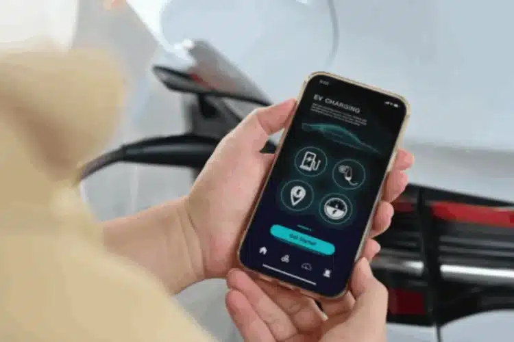 A person's hands holding a smartphone displaying an EV charging app, with an electric car in the background, symbolizing Javascript automotive app development.