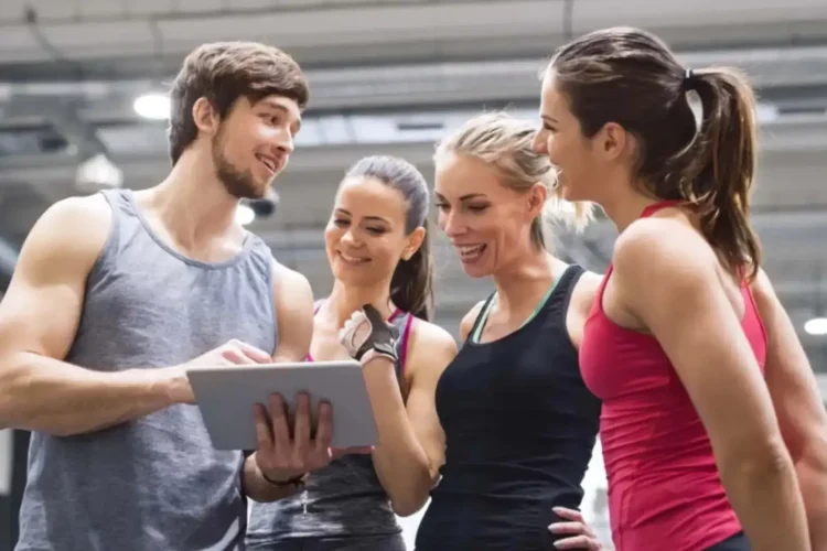 Group of people at the gym using a digital fitness platform on a tablet to track workouts and training progress.
