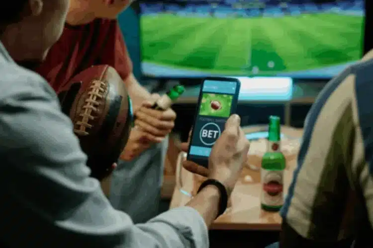 Friends watching sports and using a betting app on a smartphone, representing React Native sports app development.