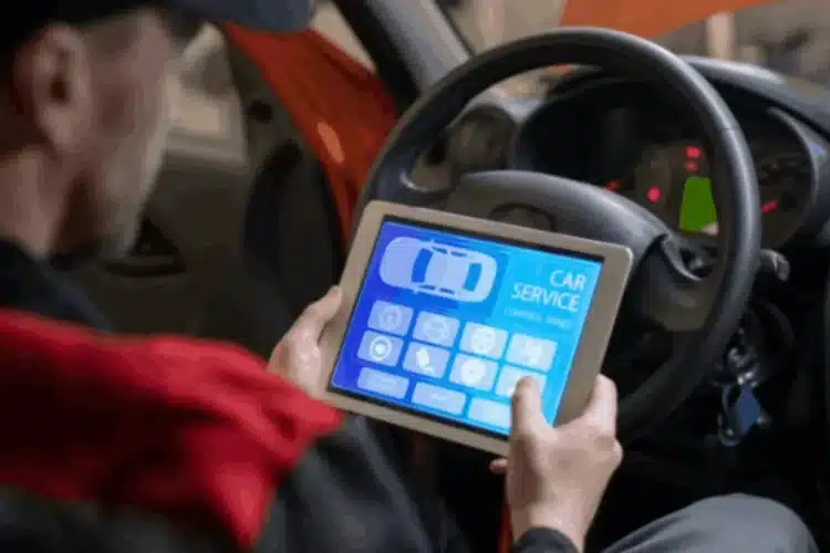 A mechanic uses a tablet with a car service app, representing an automotive telematics platform.