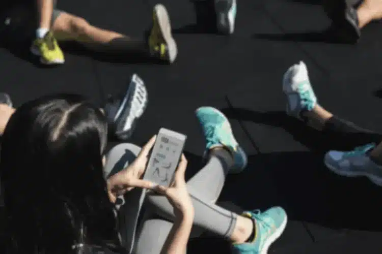 Group of people stretching while checking progress on phone, showing strong fitness app user engagement.