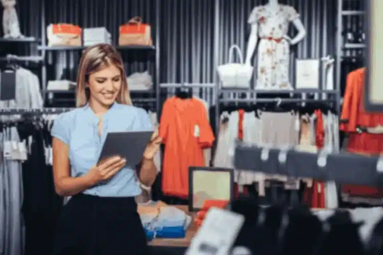 A smiling retail worker uses a tablet in a store, highlighting a retail ecommerce solution.