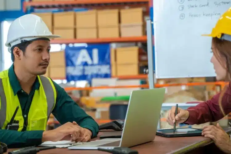 Warehouse workers discussing Python logistics automation solutions on a laptop and tablet to optimize supply chain operations.