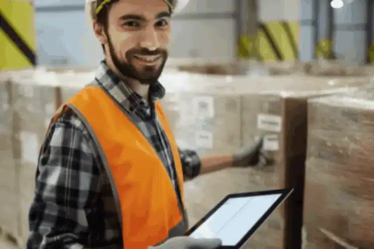 A logistics manager in a warehouse smiles, holding a tablet to manage inventory with a logistics management system.