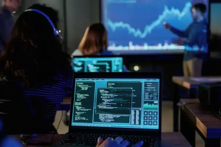 Finance risk management training with professionals analyzing data on laptops and projected stock market charts.
