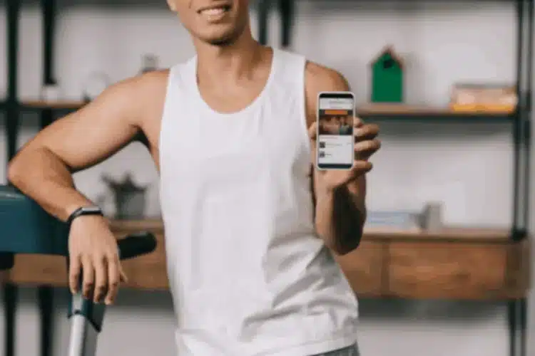 A smiling person in athletic wear holding up a smartphone displaying a fitness app, demonstrating the application of React Native in fitness app development.