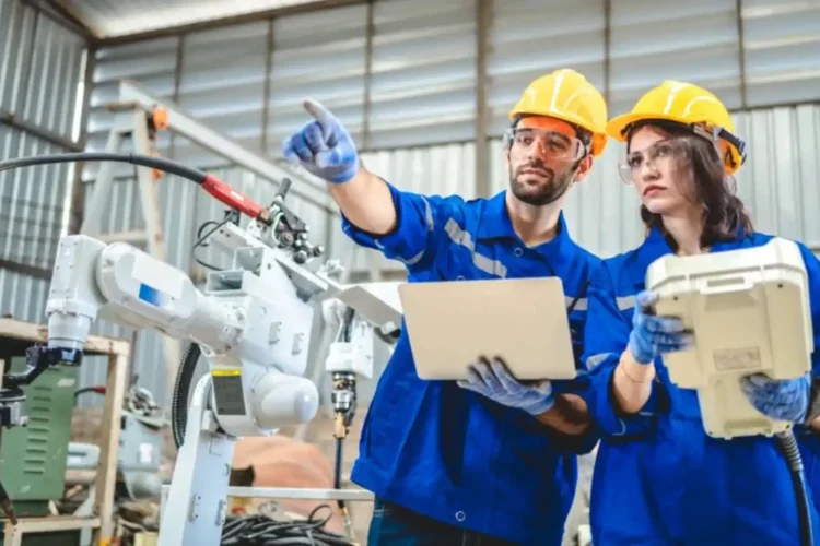 Engineers using laptops and control devices to operate robotic arms in a factory, showcasing Smart Manufacturing with Python automation.