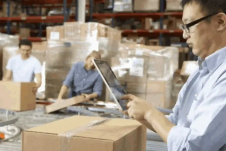 Worker using tablet to manage packages in warehouse, showcasing efficient logistics iOS app solution.