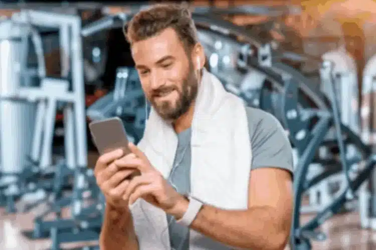 Smiling man using his phone at the gym, representing Fitness app user engagement and retention.