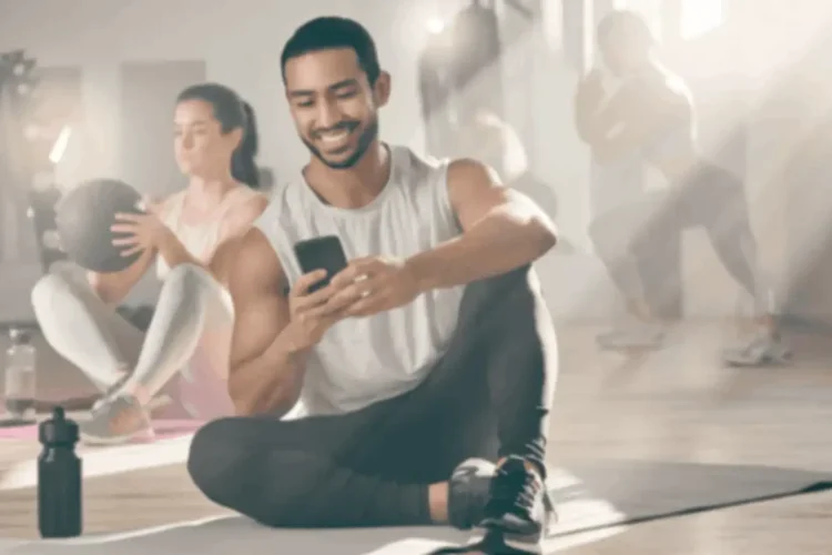 Man smiling at phone in gym, showing benefits of fitness app development for workout engagement.