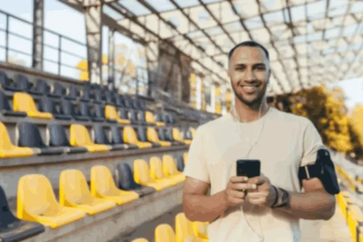 Smiling man using his phone in a stadium, symbolizing mobile app testing and Game Performance Testing.