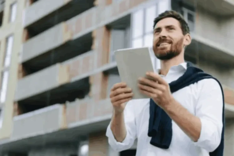 Smiling man using tablet near building, highlighting benefits of real estate app development solutions.