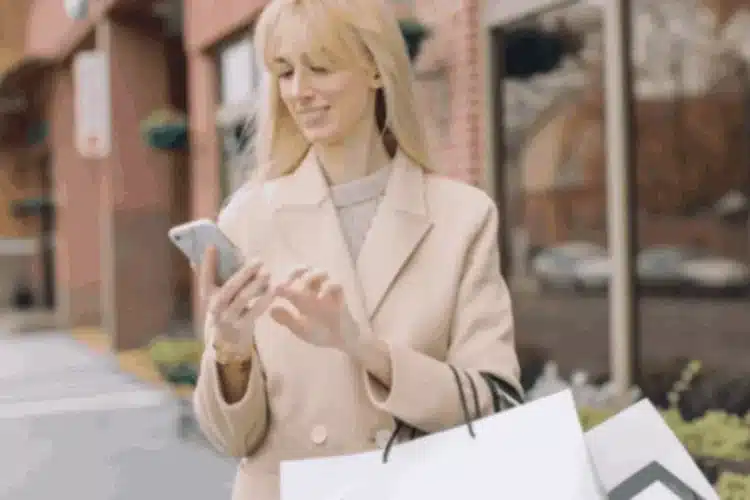 Woman holding shopping bags and using her phone, representing a Seamless Shopping Experience and high conversions.