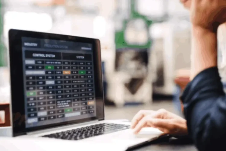 A worker uses a custom manufacturing app solution on a laptop in a factory setting.