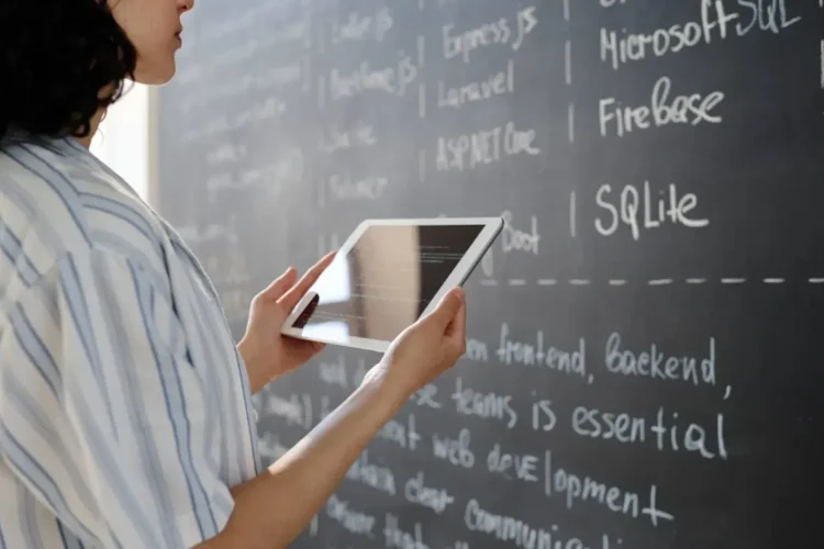 Woman holds a tablet in front of a chalkboard with text about eLearning database development.