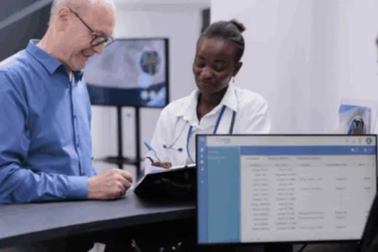 Patient and healthcare staff at a reception desk, showing a screen with patient records for EHR system accuracy.