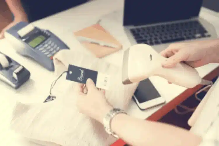 A person scans a clothing tag with a barcode reader at a retail counter. Online Checkout Reliability.